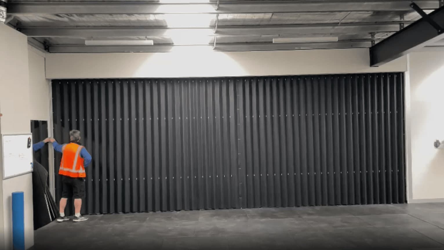 An installer drawing a black vinyl accordion door closed across a wide commercial opening