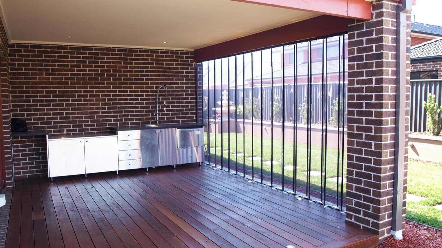 Clear folding outdoor blinds stacked back against a brick pier, opening a covered alfresco deck to the garden